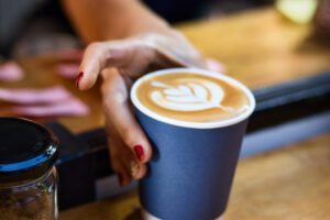 Ein Cappuccino im blauen Pappbecher wird serviert