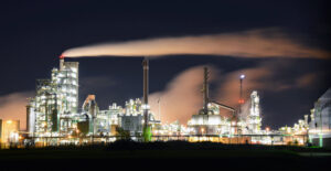 Moderne Industrieanlage bei Nacht mit rauchenden Schornsteinen