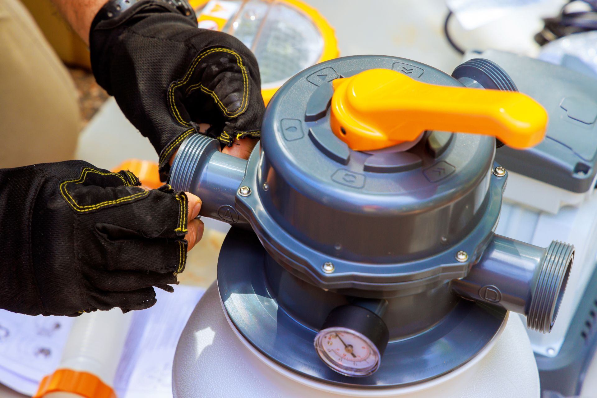 Person mit Arbeitshandschuhen montiert Anschluesse an einer Sandfilteranlage fuer den Pool